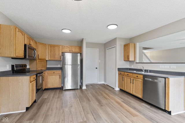 kitchen with appliances with stainless steel finishes, a sink, light wood-style floors, dark countertops, and a textured ceiling