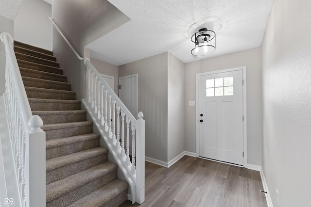 foyer entrance featuring baseboards, stairway, wood finished floors, and a textured ceiling