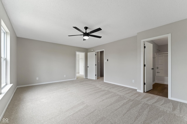 unfurnished bedroom with carpet floors, a spacious closet, baseboards, a textured ceiling, and ensuite bathroom