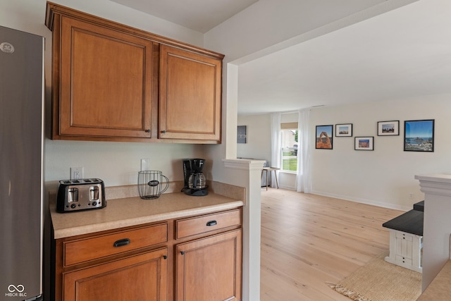 8238 Crackling Ln, Indianapolis, IN 46259 - kitchen featuring freestanding refrigerator, light wood-style floors, light countertops, brown cabinetry, and baseboards