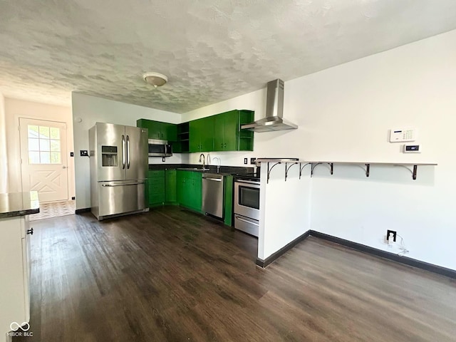 kitchen with wall chimney exhaust hood, appliances with stainless steel finishes, green cabinetry, dark countertops, and dark wood finished floors