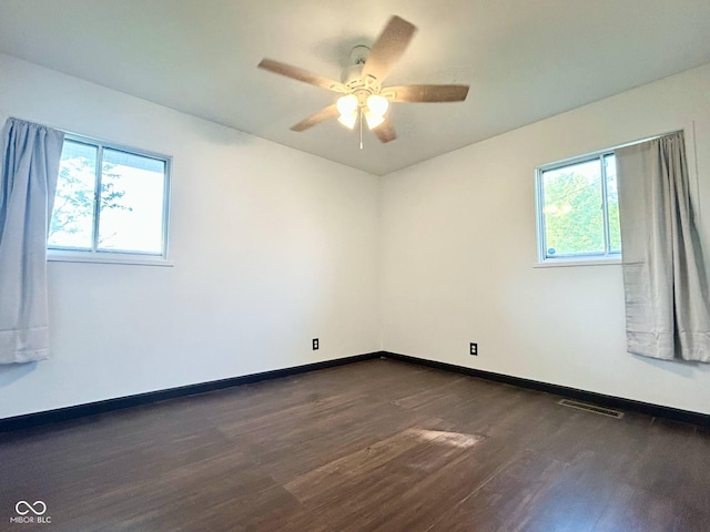 empty room featuring dark wood-style floors, healthy amount of natural light, ceiling fan, and baseboards