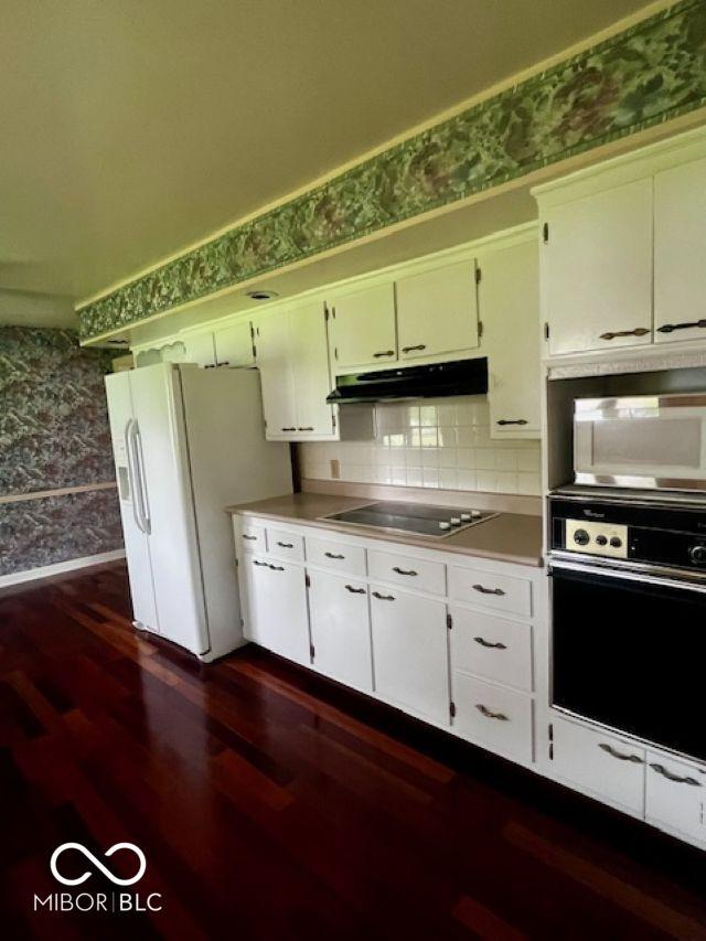5141 Derome Dr, Fort Wayne, IN 46835 - kitchen with black appliances, under cabinet range hood, wallpapered walls, dark wood-style flooring, and tasteful backsplash