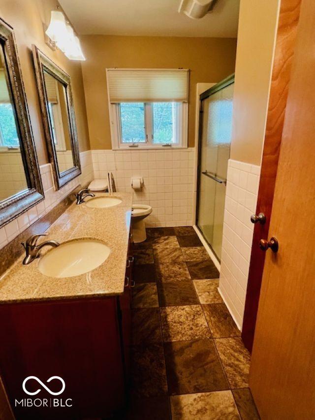 5141 Derome Dr, Fort Wayne, IN 46835 - full bathroom featuring tile walls, double vanity, a shower stall, toilet, and a wainscoted wall