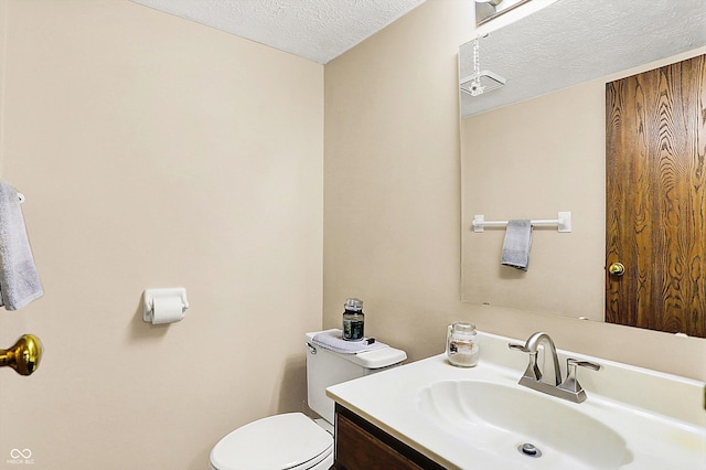 half bath featuring a textured ceiling, toilet, and vanity