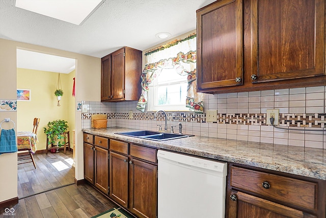 kitchen with white dishwasher, a sink, baseboards, dark wood-style flooring, and tasteful backsplash