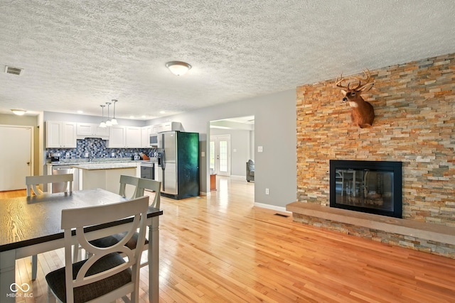 6462 Wings Ct, Brownsburg, IN 46112 - dining space with light wood-type flooring, a textured ceiling, a fireplace, and baseboards