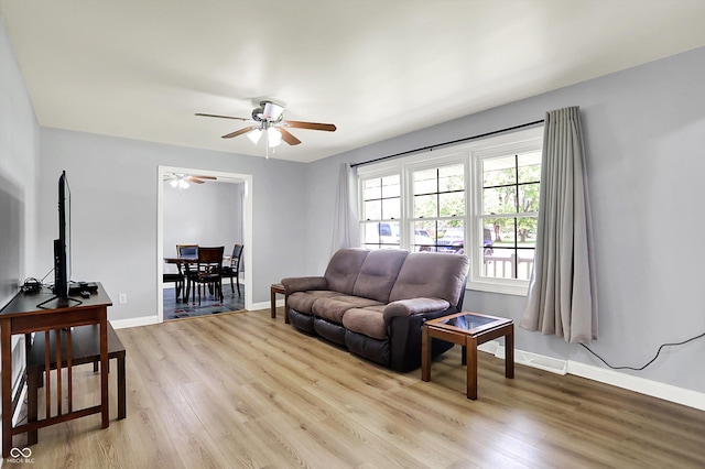 living room with light wood-type flooring, a ceiling fan, and baseboards