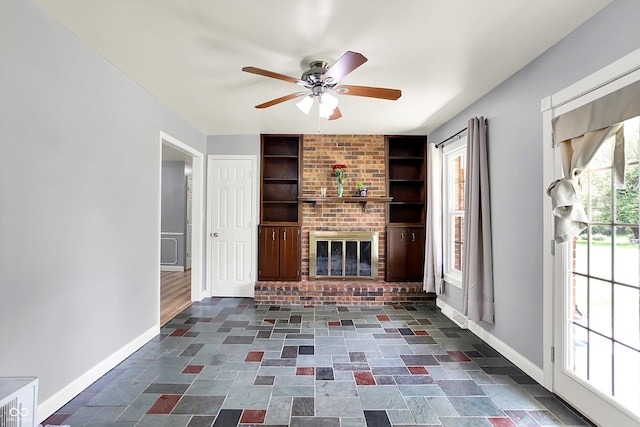 unfurnished living room featuring baseboards, a ceiling fan, built in shelves, and a brick fireplace
