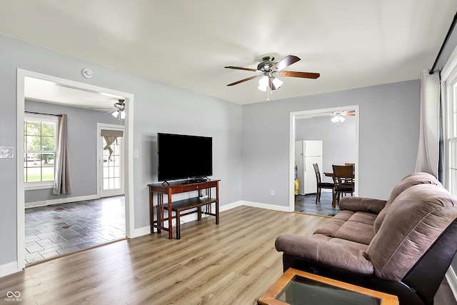living area with a ceiling fan, baseboards, and light wood-style flooring