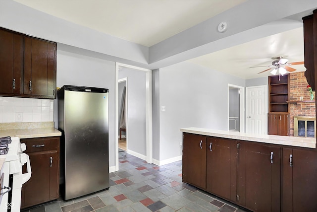 kitchen featuring freestanding refrigerator, gas range, light countertops, dark brown cabinetry, and ceiling fan