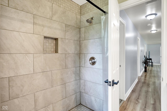 full bathroom with tiled shower, wood finished floors, and baseboards