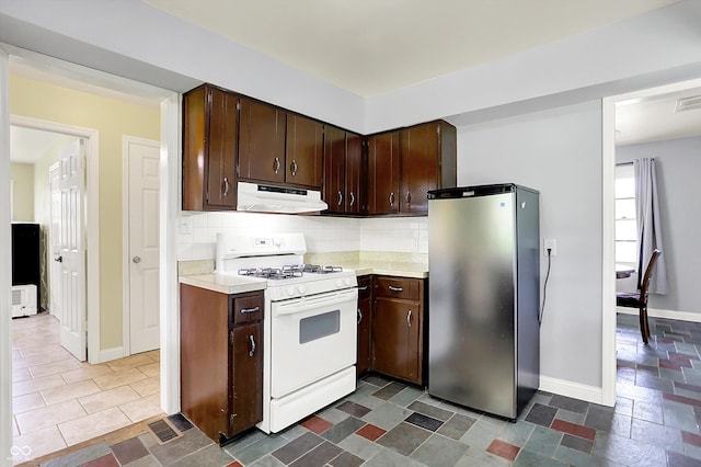 kitchen featuring freestanding refrigerator, white gas stove, under cabinet range hood, and light countertops