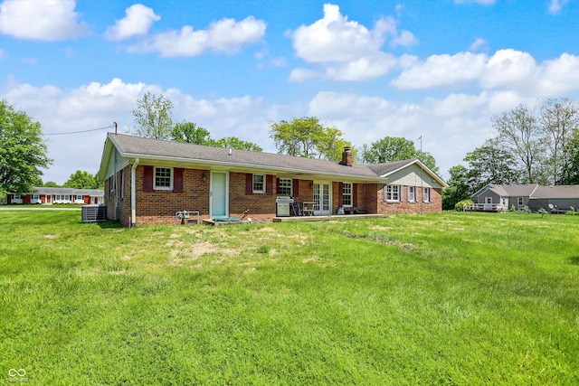view of front of house featuring brick siding, a chimney, a front yard, and central AC