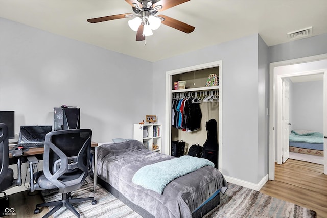 bedroom featuring wood finished floors, a closet, a desk, baseboards, and ceiling fan