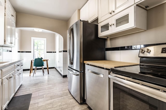 5428 E 10th St, Indianapolis, IN 46219 - kitchen with stainless steel appliances, arched walkways, light wood finished floors, white cabinetry, and glass insert cabinets