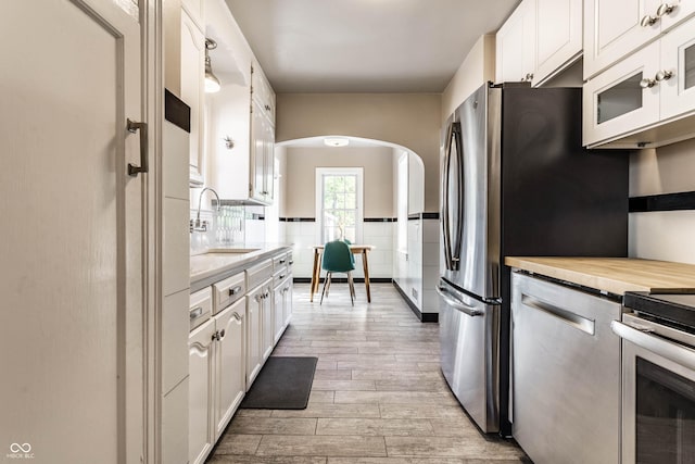 5428 E 10th St, Indianapolis, IN 46219 - kitchen featuring arched walkways, a sink, light wood-style flooring, white cabinetry, and stainless steel appliances
