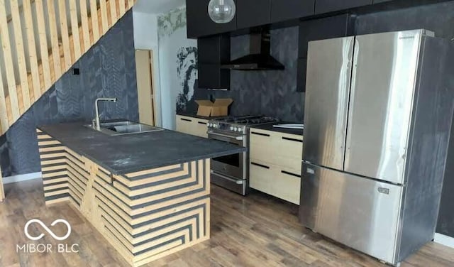 kitchen with stainless steel appliances, wall chimney range hood, a sink, dark countertops, and wood finished floors