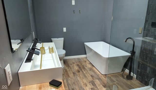 bathroom with wood finished floors, toilet, a freestanding tub, and baseboards