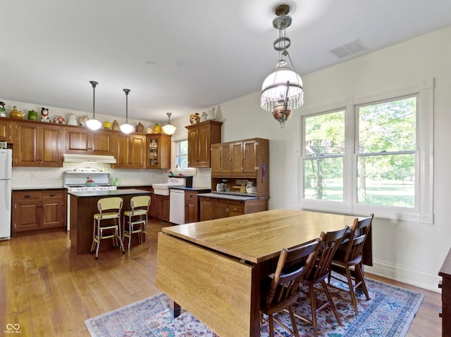 19702 Centennial Rd, Sheridan, IN 46069 - kitchen featuring under cabinet range hood, white appliances, brown cabinets, a center island, and decorative backsplash