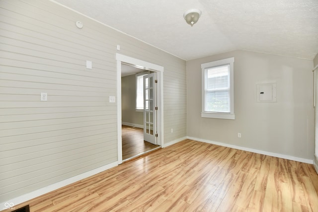 631 Prospect St, Indianapolis, IN 46203 - spare room with light wood-style flooring, electric panel, wooden walls, vaulted ceiling, and a textured ceiling