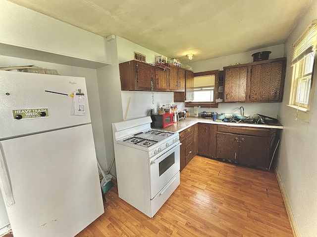 kitchen featuring white appliances, light wood finished floors, light countertops, a sink, and dark brown cabinets