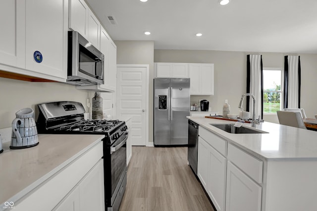 kitchen with appliances with stainless steel finishes, a sink, white cabinetry, light wood finished floors, and light countertops