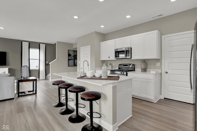kitchen with appliances with stainless steel finishes, open floor plan, light wood-style floors, an island with sink, and white cabinets