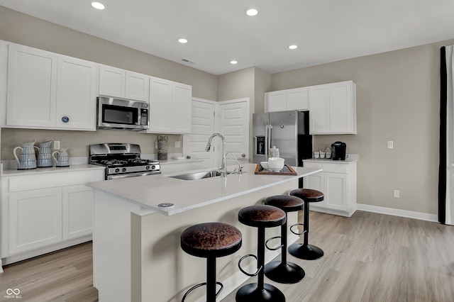kitchen featuring appliances with stainless steel finishes, a sink, a kitchen bar, light wood-style floors, and white cabinets