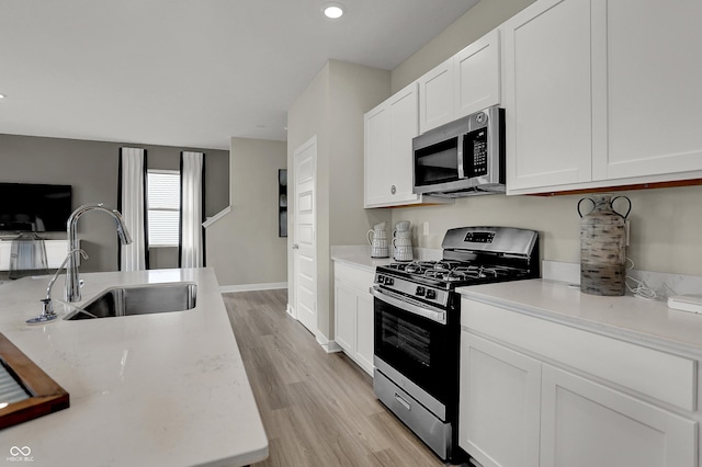 kitchen with appliances with stainless steel finishes, a sink, white cabinetry, light wood-style floors, and recessed lighting