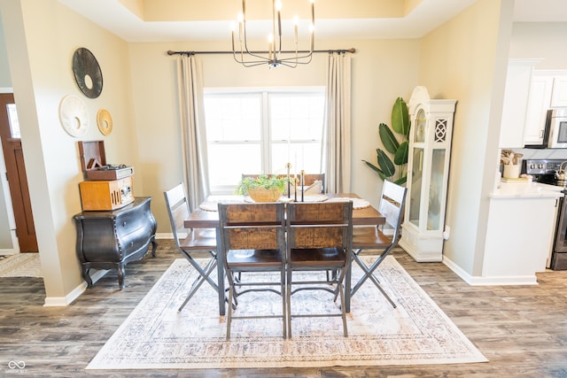 dining room with a chandelier, wood finished floors, baseboards, and a tray ceiling
