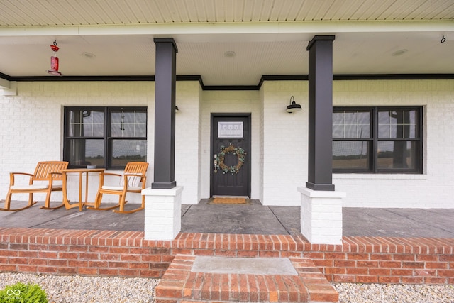 entrance to property featuring a porch and brick siding