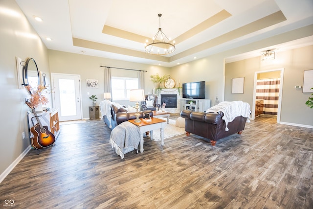 living area with a tray ceiling, wood finished floors, a chandelier, and recessed lighting