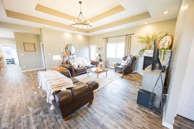 living area featuring a raised ceiling, wood finished floors, a chandelier, baseboards, and recessed lighting