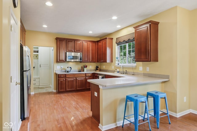 9311 Windrift Way, Zionsville, IN 46077 - kitchen featuring appliances with stainless steel finishes, a peninsula, light wood finished floors, light countertops, and a breakfast bar area