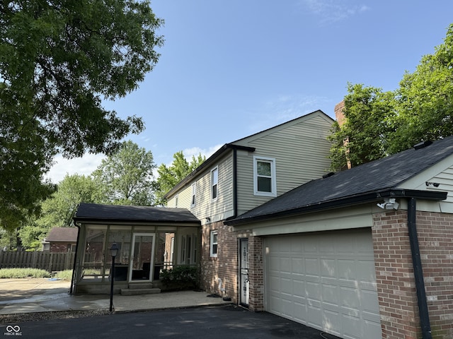5433 Brendonridge Rd, Indianapolis, IN 46226 - view of home's exterior featuring a sunroom, an attached garage, fence, brick siding, and asphalt driveway