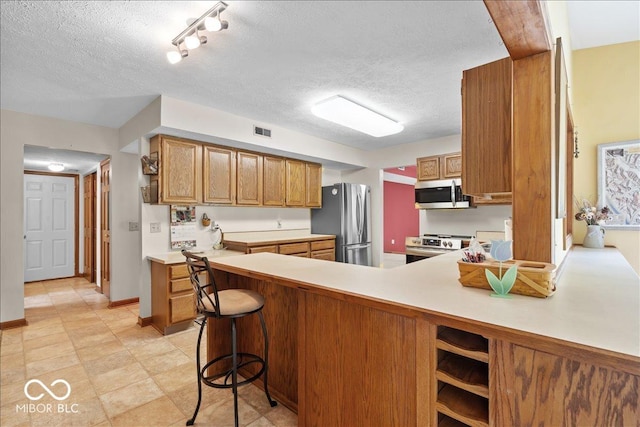 14814 Beacon Blvd, Carmel, IN 46032 - kitchen with appliances with stainless steel finishes, light countertops, a peninsula, brown cabinets, and a textured ceiling