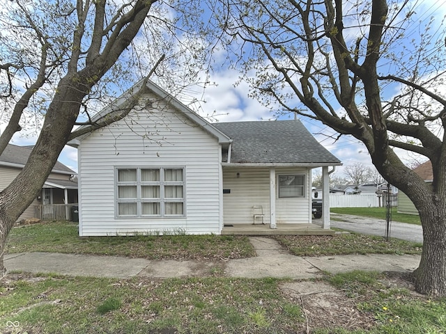 bungalow-style home with roof with shingles, a porch, and fence