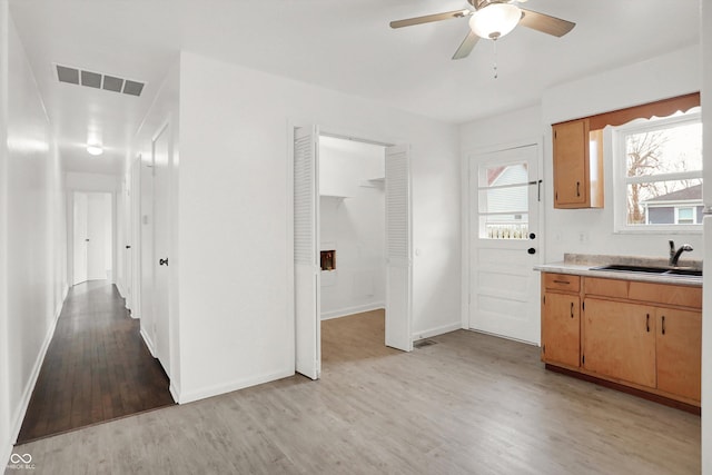 kitchen featuring a sink, light wood-style floors, light countertops, ceiling fan, and baseboards