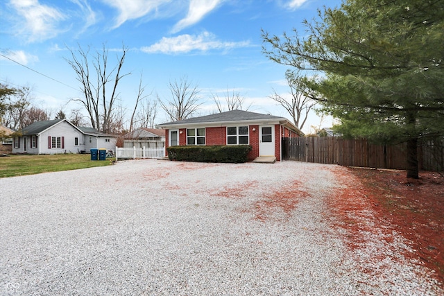 ranch-style home featuring gravel driveway, fence, and brick siding