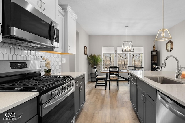 3583 Collier Dr, Lafayette, IN 47905 - kitchen with appliances with stainless steel finishes, a sink, light wood-style flooring, tasteful backsplash, and hanging light fixtures