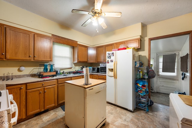 kitchen with white fridge with ice dispenser, a ceiling fan, light countertops, brown cabinetry, and a kitchen island