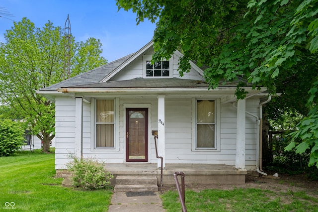 view of front of home with a shingled roof, a front lawn, and covered porch