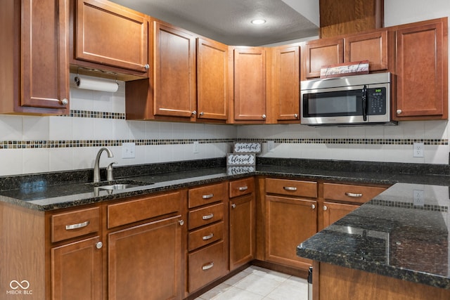 3449 Brixford Ln, West Lafayette, IN 47906 - kitchen with stainless steel microwave, a sink, backsplash, light tile patterned floors, and dark stone counters