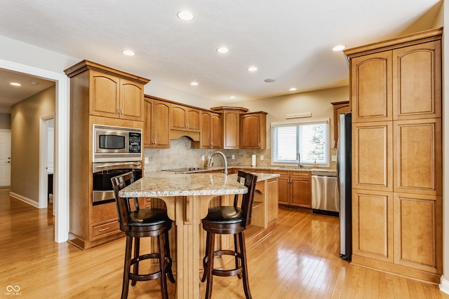 10784 Giselle Way, Fishers, IN 46040 - kitchen featuring stainless steel appliances, light wood-style floors, an island with sink, a kitchen breakfast bar, and light stone counters