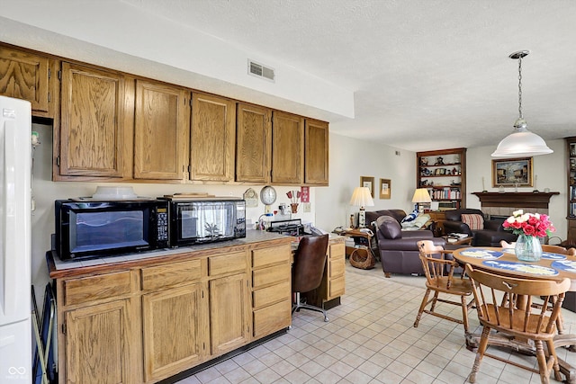 kitchen featuring a textured ceiling, decorative light fixtures, open floor plan, brown cabinets, and freestanding refrigerator