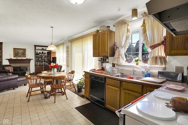 kitchen with dishwasher, a sink, brown cabinetry, a tiled fireplace, and decorative light fixtures