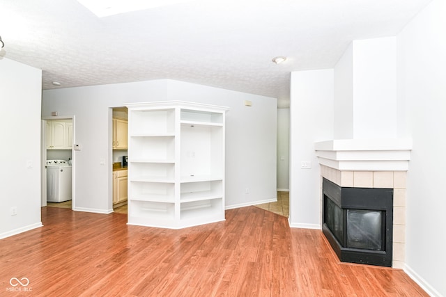 1030 Longwell Pl, Indianapolis, IN 46240 - unfurnished living room with light wood-style flooring, a tile fireplace, baseboards, washer and clothes dryer, and a textured ceiling