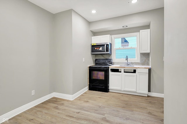1033 N Dearborn St, Indianapolis, IN 46201 - kitchen featuring black range with electric stovetop, stainless steel microwave, white cabinets, light wood-style flooring, and a sink
