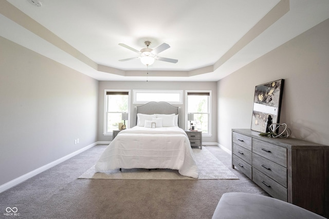 bedroom featuring light carpet, a tray ceiling, baseboards, and ceiling fan